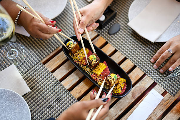Top view of hands with chopsticks sharing a dish of crispy pork belly served with corn on a wooden lunch table