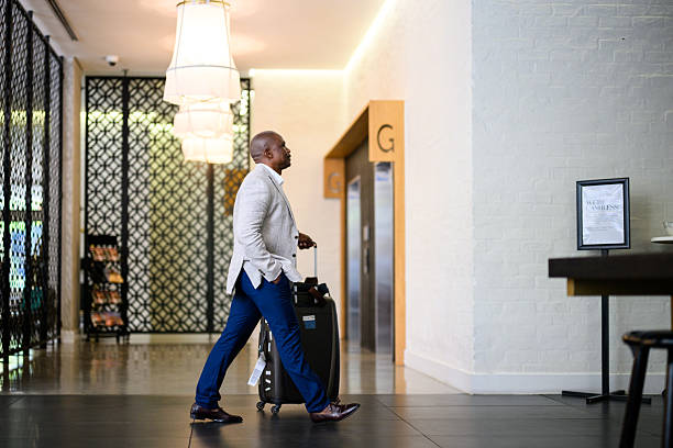 istock Side view of a business man pulling his suitcase and walking through a modern hotel lobby with modern interior decor and pendant lights 2238275033