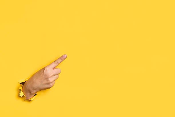 istock Female hand pointing  empty copy space  through hole in torn yellow paper background 2238281302