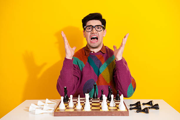 istock Frustrated young man wearing glasses holding hands up with a dramatic expression, sitting in front of a chess board 2238282824