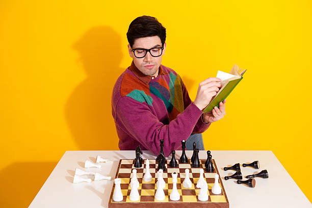 istock Young man in colorful sweater reading a book while playing chess against a vibrant yellow background 2238282842