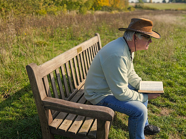 istock Elderly man wearing a leather hat reading a book on a park bench 2238283309