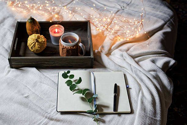 A relaxing space with a wellness diary opened on a soft blanket. A cup of warm tea, a candle, and decorative gourds create a peaceful atmosphere perfect for reflection and journaling. Copy space for text, high angle view - Mindfulness, mental awareness