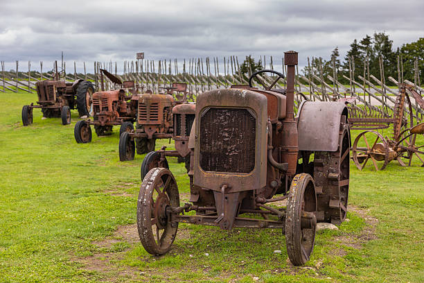 Saaremaa, Estonia. A collection of old rusty tractors and farming equipment displayed on a green field with wooden fences.