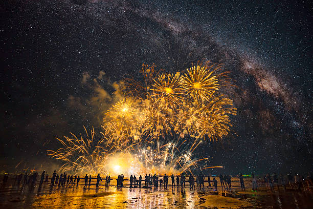 Silhouetted crowd, golden fireworks, and Milky Way.