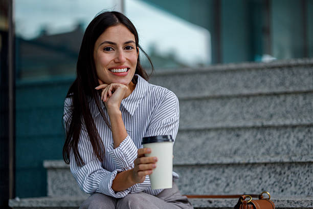 istock Professional woman taking a coffee break on outside stairs, holding a disposable cup, feeling happy and confident 2238295584