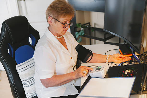 istock An elderly woman measures her blood pressure while working in her home office. 2238298199