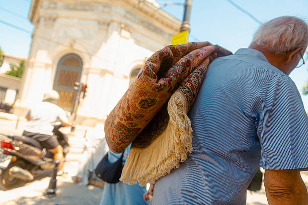Close-up of a man carrying a rolled traditional carpet on his shoulder in a vibrant urban street scene, symbolizing craftsmanship and everyday life in Istanbul city center.