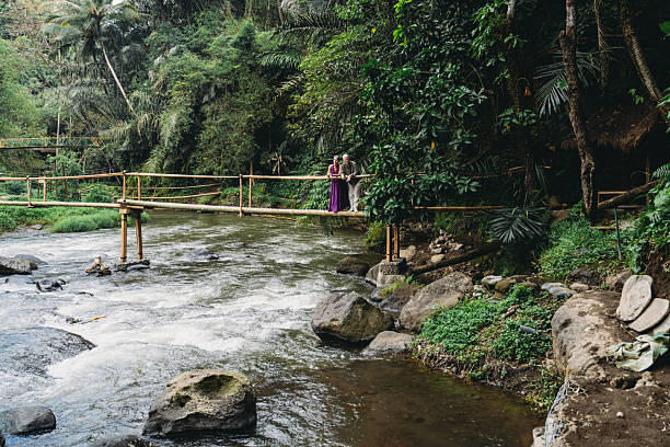 Mature couple standing on a bamboo bridge, enjoying a peaceful walk over a river in a lush tropical jungle