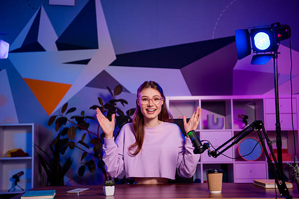 istock Young female blogger in modern studio recording a live podcast using a microphone amidst vibrant lighting decor 2238299510