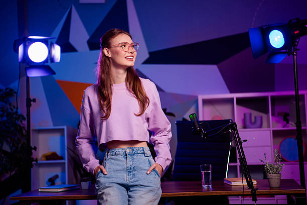 istock Young female content creator in stylish casual attire preparing for a live stream with vibrant neon lights in a modern setup 2238299615