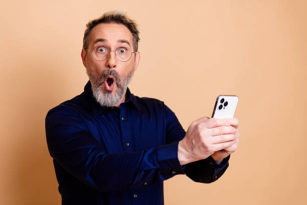 istock Young professional man captivated by smartphone with surprise on light beige background 2238300242