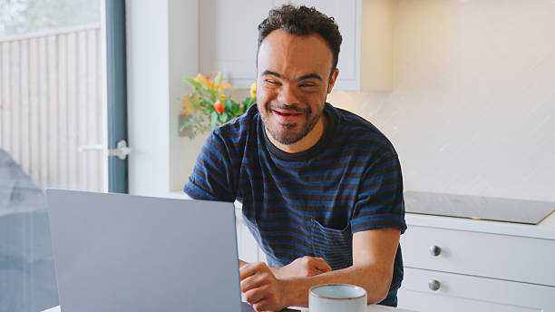 Man With Down Syndrome At Home Working On Laptop On Kitchen Surface
