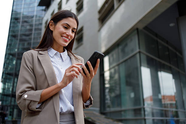 istock Businesswoman standing in city, using smartphone, smiling and scrolling for work or communication 2238303636