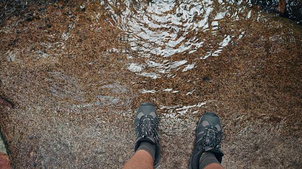Variety shots from the POV of man’s legs as they step through different surfaces - dirt, mud, water, sand, gravel, rocky paths, grass, water and pavement. Camera captures movement of the legs as they travel through terrain.