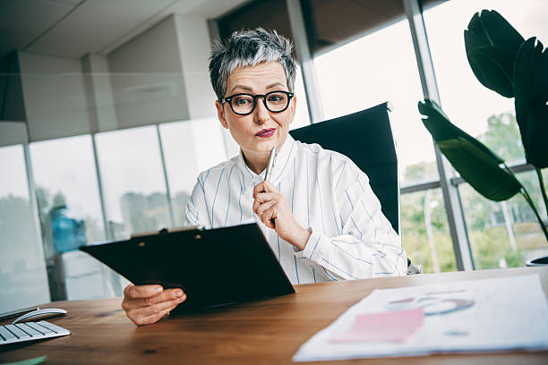 istock Confident businesswoman in a modern office analyzing work documents with a clipboard, representing professional success 2238305210