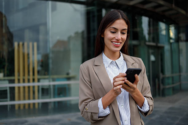 istock Young businesswoman smiling, using mobile phone for communication outside office building in a city setting 2238306504