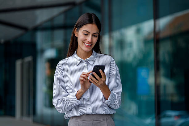 istock Businesswoman smiling, typing on phone, standing outside modern office building, using mobile technology for communication 2238306625