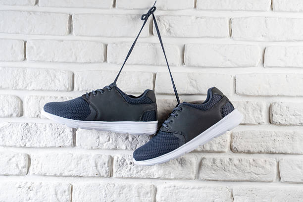 Pair of Black Sneakers Hanging on White Brick Wall