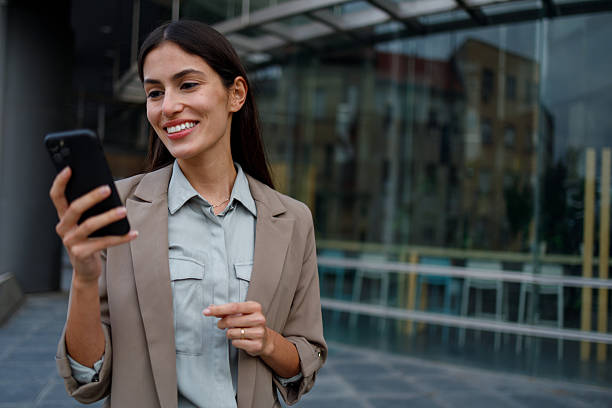 istock Businesswoman standing in city, smiling while using smartphone for communication and networking 2238307281