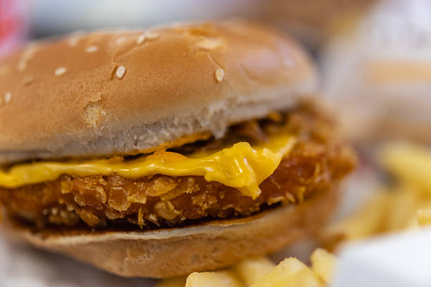 close-up of a crispy fried chicken or pork sandwich on a sesame bun with melted cheese, served with blurry french fries for a perfect fast-food meal