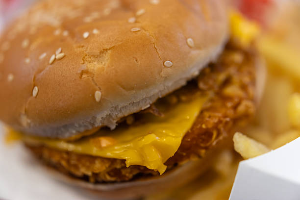 close-up of a crispy fried chicken or pork sandwich on a sesame bun with melted cheese, served with blurry french fries for a perfect fast-food meal
