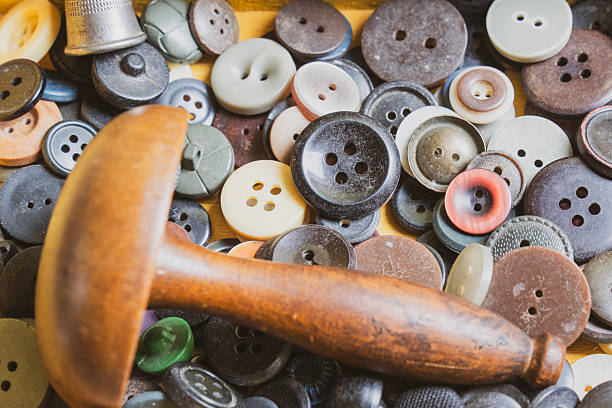 A close-up view of assorted sewing supplies including colorful buttons, spools of thread, thimbles, and a wooden darning tool. The image conveys a nostalgic and handmade atmosphere, highlighting traditional craftsmanship and domestic creativity.