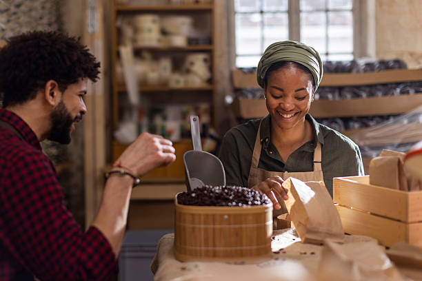 istock Smiling Artisan in Apron Packs Fresh Coffee Beans While Co-Worker Scoops in a Busy Workshop 2238334188