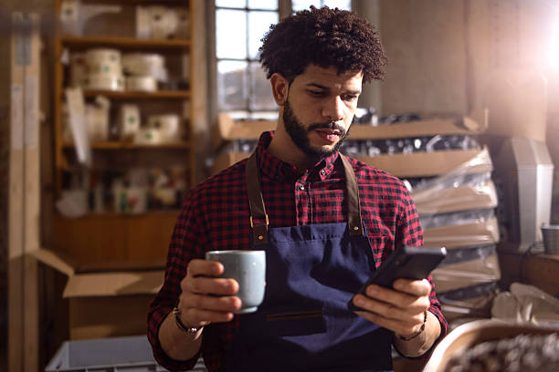 istock Craftsman In Apron Checks Phone While Holding Coffee Mug In Workshop Studio During Morning Break 2238334207