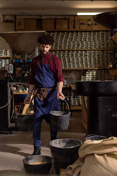 Worker In Apron Carrying Buckets In Industrial Workshop At Coffee Roastery