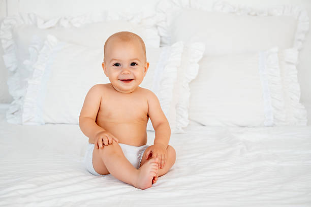 a baby in a diaper on a white bed, space for text, a small, smiling child sitting on a bed at home.