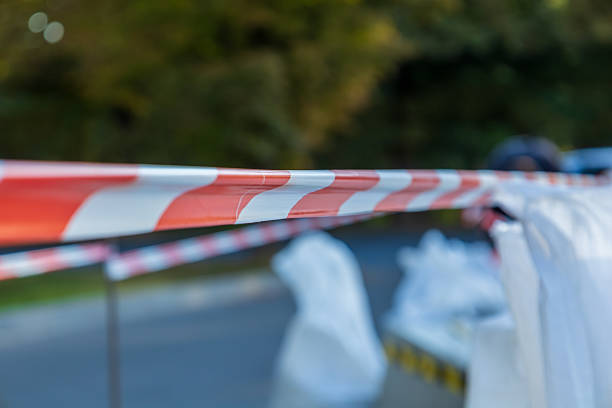 Bright red and white caution tape secures a restricted area in a park as officials assess the situation during daylight hours.