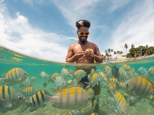 istock Afro man bathing with fish on a tropical beach 2238372032