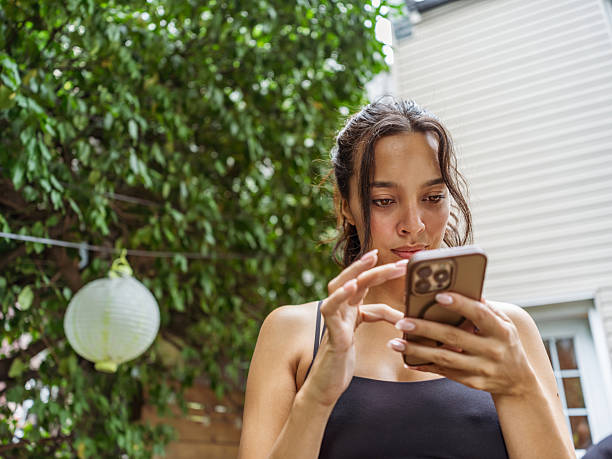 Young multiracial expecting woman texting on the patio in back yard. She is dressed in sport clothing.  Exterior of backyard patio at private home in Toronto, Canada.