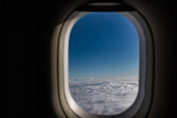View through an aircraft window showing endless layers of white clouds under a bright blue sky. The soft natural light and perspective evoke feelings of calmness, travel, and the wonder of flying at high altitude.