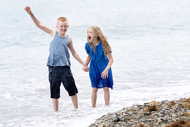 Children playing with the waves on the sea or ocean coast during a family vacation. Peaceful tropical summer holiday, travel, relaxation, summer vacation,