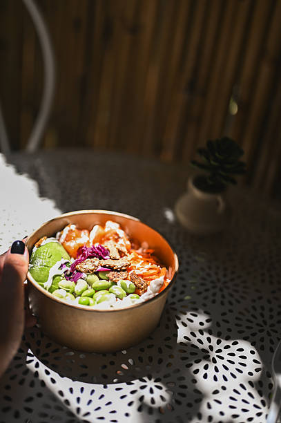 istock Hand holding poke bowl on outdoor table with dappled sunlight 2238384323