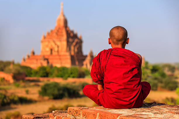 Young Buddhist monk sitting on the temple and looking at the view of ancient Bagan, Myanmar (Burma)