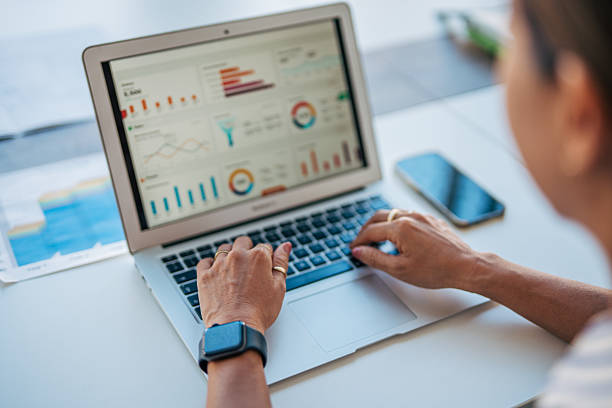 Woman's hands typing on a laptop, displaying various business charts and analytics dashboards on the screen, reflecting modern data analysis and technology in a professional setting