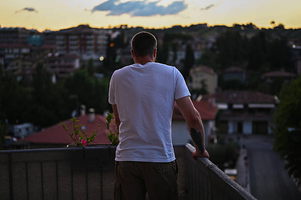Man standing on a balcony overlooking a city view at sunset, feeling thoughtful and contemplative