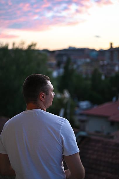 Man looking at the city skyline during a colorful sunset, finding a peaceful moment