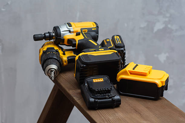 istock Professional cordless power tool set with yellow and black drill, impact driver, and lithium-ion batteries on wooden surface. 2238405168