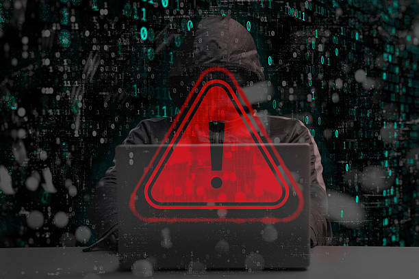 istock A hooded hacker behind a laptop with a red glowing warning with a triangle and exclamation mark. Binary code overlays the scene, emphasizing the concept of data leakage and cybercrime. 2238406004