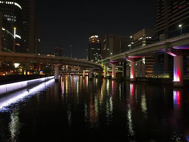 Night view of a cityscape with illuminated bridges and buildings reflecting on a river.