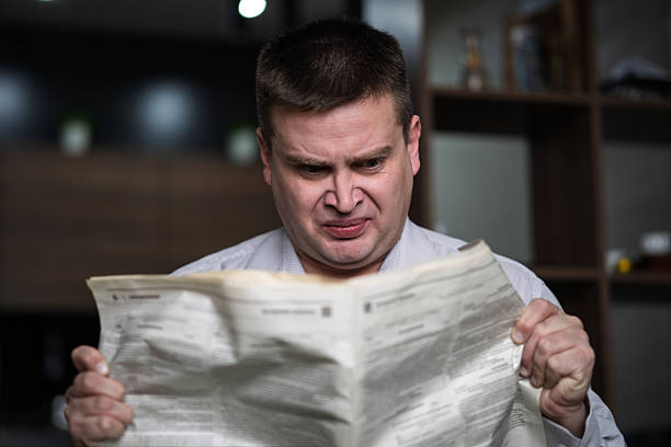 istock Smiling mature man reading newspaper while sitting at the table on dark background. Guy crumple newspaper 2238425619