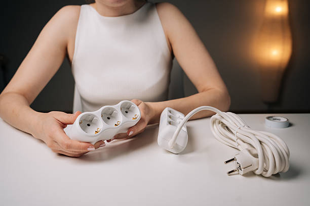 istock Woman holding white triple electrical socket in her hands, sitting at desk with another socket next to her, close-up. Concept of electrical solutions 2238426488