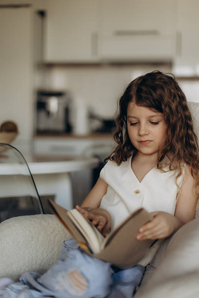 istock Young Girl Sitting Indoors Reading a Book While Smiling 2238434660