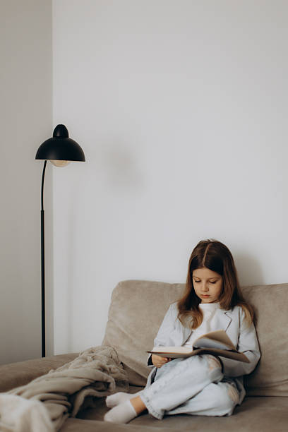 istock Young Girl Sitting on a Couch Reading a Book with Focus 2238434664