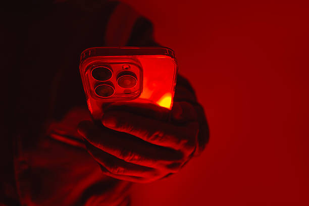istock Close-up of a man's hand holding a modern smartphone under bright red studio lighting. Concept of digital cybersecurity, data privacy, hacker activity and darknet. 2238448863