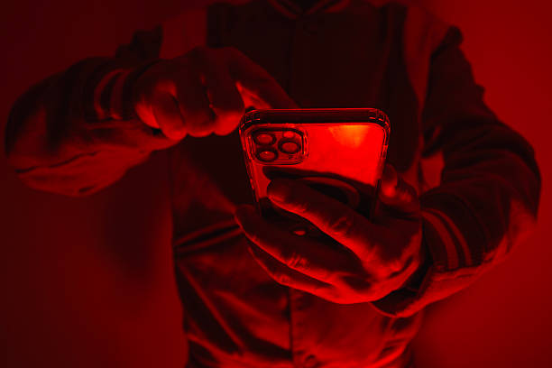 istock Close-up of a man's hand holding a modern smartphone under bright red studio lighting. Concept of digital cybersecurity, data privacy, hacker activity and darknet. 2238448869